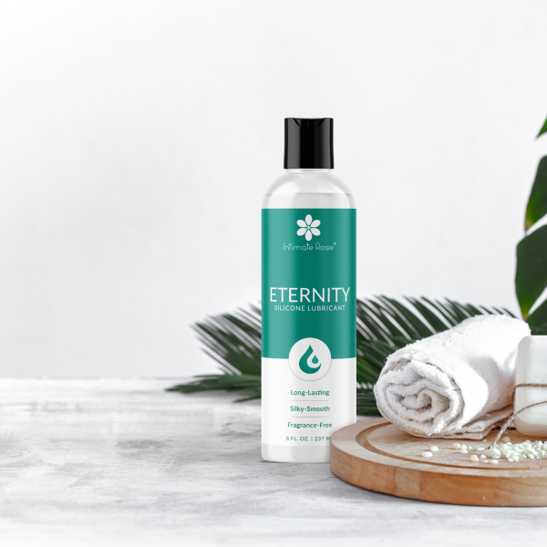 A bottle of Intimate Rose® Eternity Silicone Lubricant beside a rolled towel on a wooden tray.